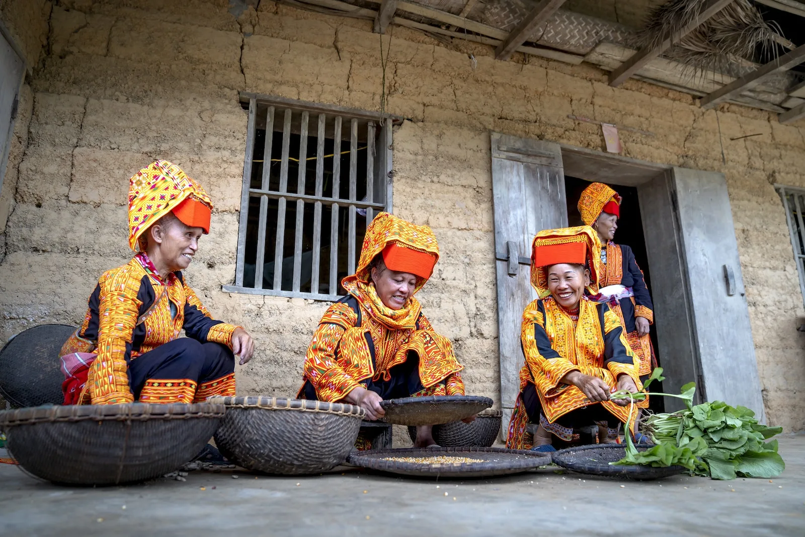 Women in Orange Traditional Clothes Working Outside a Rough Beige House